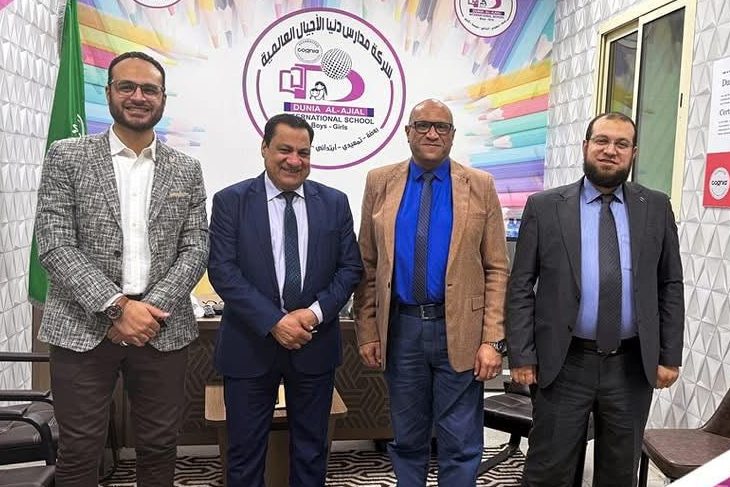 Four men standing in an office below the Dunia Al-Ajial International School logo