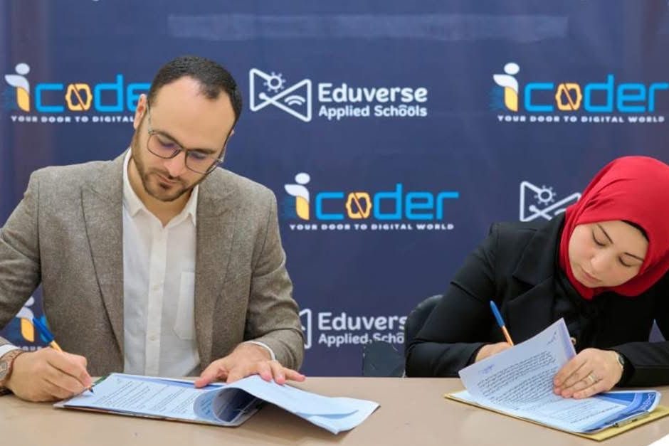 A man and a woman signing copies of an agreement at a table, in front of an iCoder and Eduverse Applied Schools backdrop