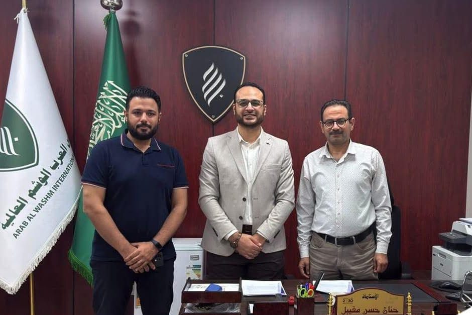 Three men standing in an office between flags, with the Arab Al Washm International Schools flag on the left